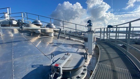 Een panoramisch uitzicht vanaf een metalen platform met ronde tanks en leidingen, onder een blauwe lucht met wolken.
