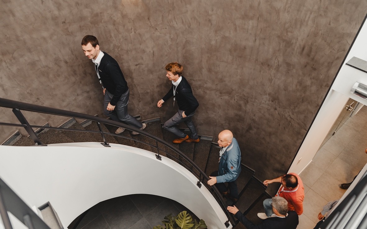 Groep mannen die een wenteltrap oplopen in een moderne omgeving.